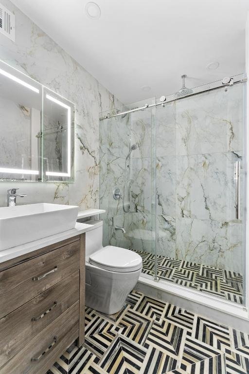 bathroom featuring vanity, a shower with shower door, and toilet