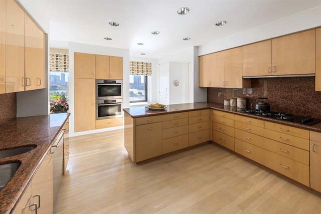 kitchen featuring stainless steel double oven, tasteful backsplash, light brown cabinetry, dark stone countertops, and black gas cooktop