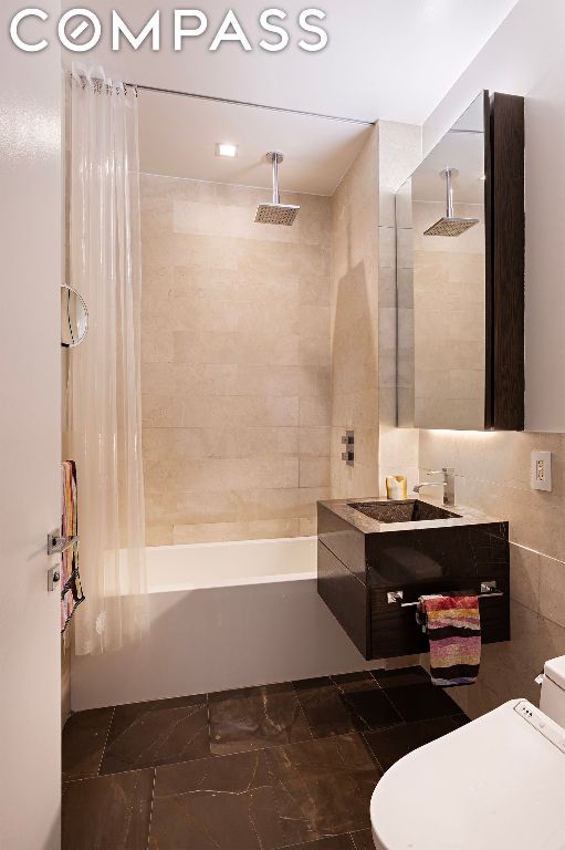 full bathroom featuring shower / tub combo with curtain, vanity, toilet, and tile walls