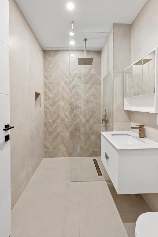 bathroom featuring vanity, toilet, tile walls, and a tile shower