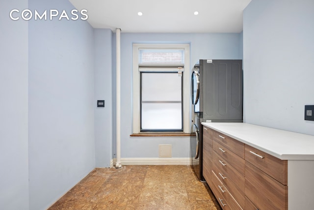 clothes washing area with baseboards, stacked washing maching and dryer, laundry area, recessed lighting, and stone finish flooring