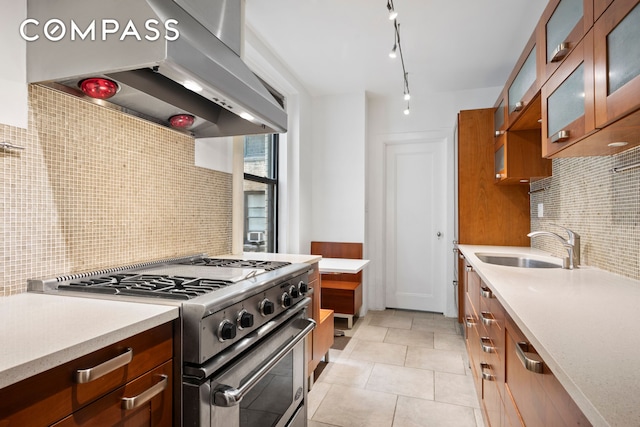 kitchen featuring under cabinet range hood, light countertops, brown cabinetry, high end stainless steel range, and a sink