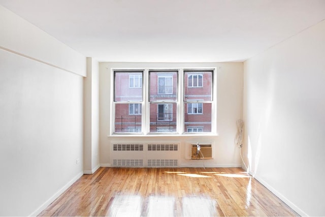 spare room with radiator, an AC wall unit, and light wood-type flooring