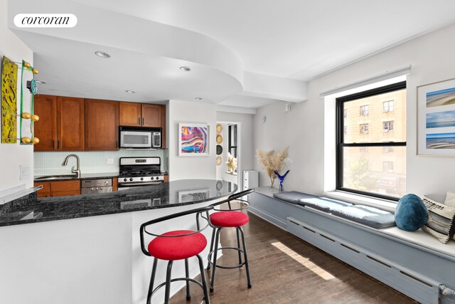 kitchen with sink, appliances with stainless steel finishes, tasteful backsplash, a kitchen bar, and a baseboard radiator