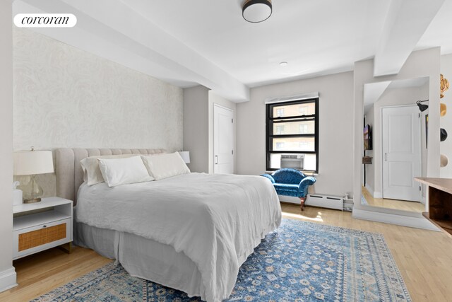 bedroom with a baseboard heating unit, cooling unit, and light hardwood / wood-style flooring