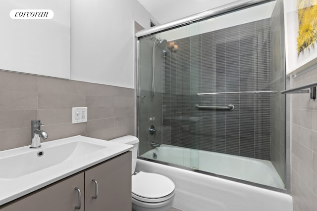 full bathroom featuring bath / shower combo with glass door, tile walls, decorative backsplash, vanity, and toilet