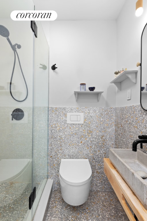 bathroom featuring toilet, sink, tile walls, a shower with door, and decorative backsplash