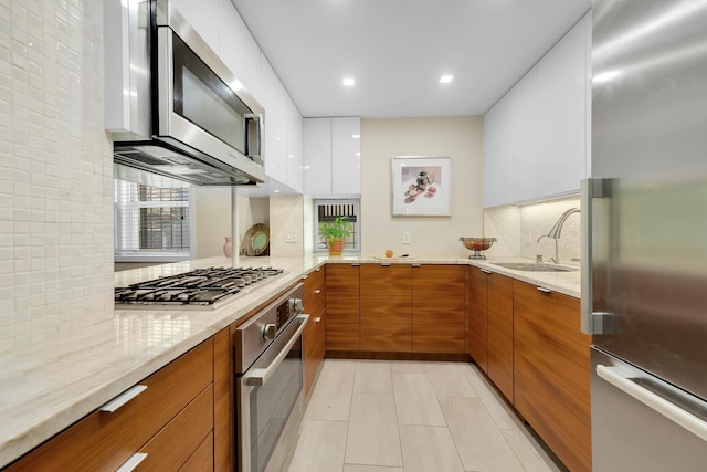 kitchen featuring stainless steel appliances, a sink, light stone countertops, brown cabinetry, and modern cabinets