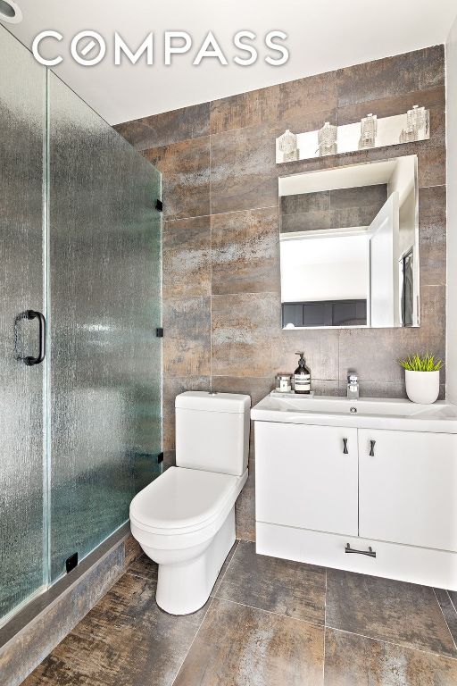 bathroom featuring walk in shower, tile walls, vanity, and toilet