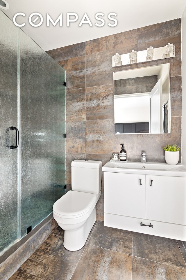 bathroom with toilet, tile walls, a stall shower, and vanity