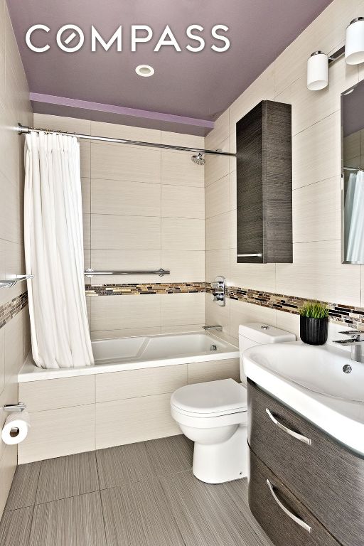 full bathroom with toilet, tile walls, vanity, shower / bath combo with shower curtain, and tile patterned flooring