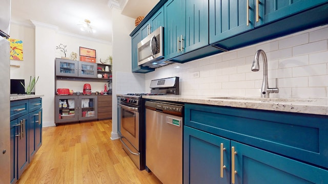 kitchen with stainless steel appliances, crown molding, blue cabinetry, and sink