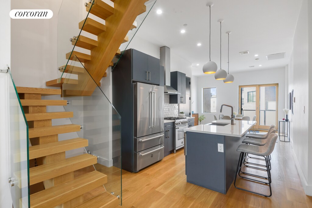 kitchen with light countertops, a kitchen island with sink, a sink, high quality appliances, and wall chimney exhaust hood