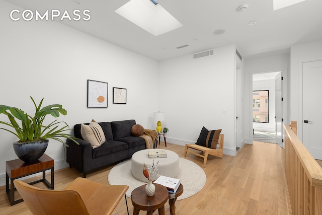 living room with light wood-style flooring, baseboards, visible vents, and a skylight