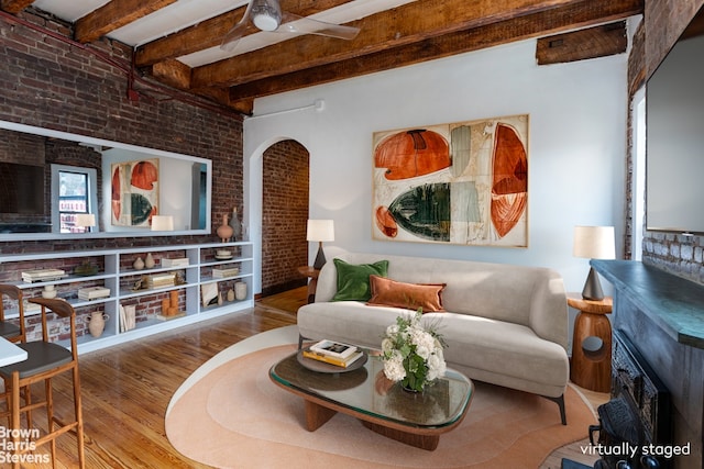 living room with brick wall, beam ceiling, ceiling fan, and wood finished floors