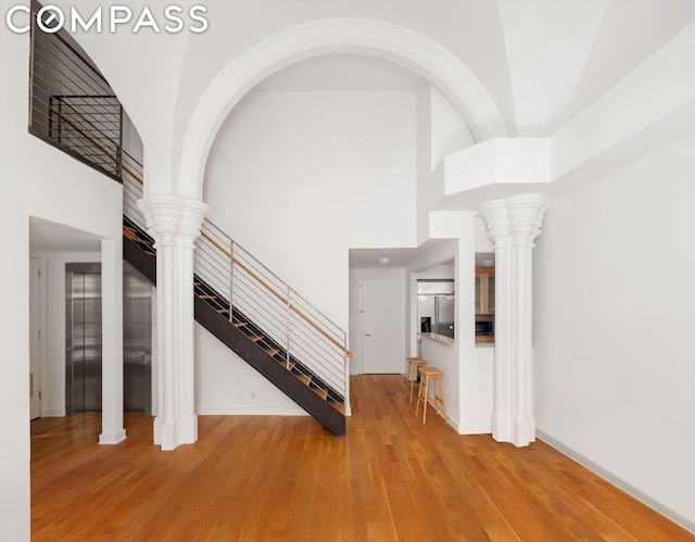 unfurnished living room with decorative columns, wood-type flooring, and a high ceiling