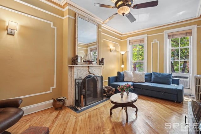 living room with hardwood / wood-style flooring, ornamental molding, ceiling fan, and a fireplace