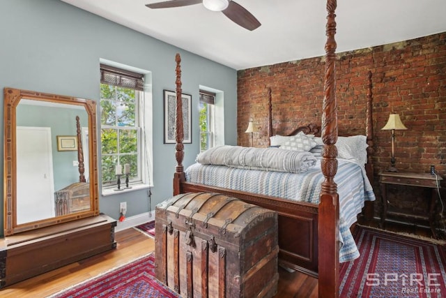 bedroom with ceiling fan, brick wall, wood-type flooring, and multiple windows