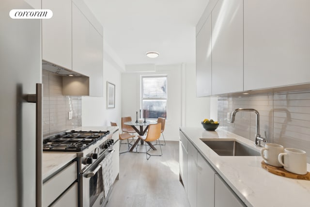 kitchen featuring sink, white cabinets, light stone counters, stainless steel range with gas stovetop, and light wood-type flooring