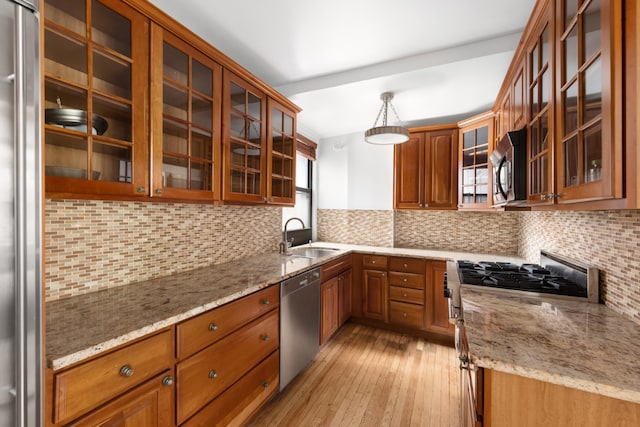 kitchen featuring appliances with stainless steel finishes, a sink, glass insert cabinets, and pendant lighting