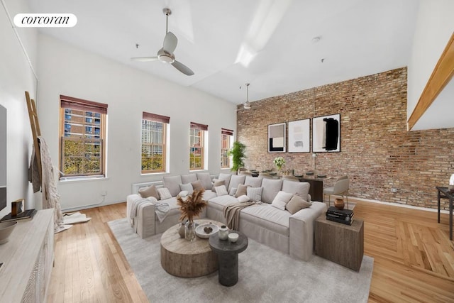 living room featuring ceiling fan, a high ceiling, brick wall, and light wood-type flooring