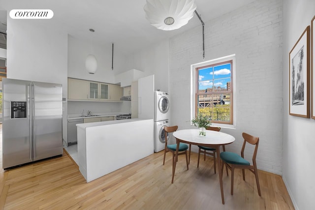 kitchen featuring light wood-style flooring, stainless steel appliances, a sink, and stacked washer and clothes dryer