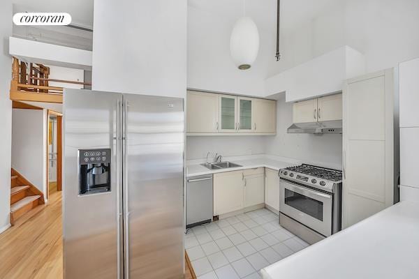 kitchen featuring under cabinet range hood, stainless steel appliances, a sink, light countertops, and glass insert cabinets