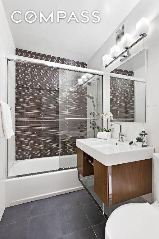 full bathroom featuring tile patterned flooring, vanity, combined bath / shower with glass door, and toilet