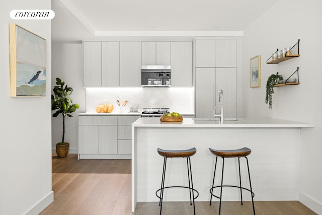kitchen featuring a breakfast bar area, modern cabinets, open shelves, a peninsula, and light wood-style floors