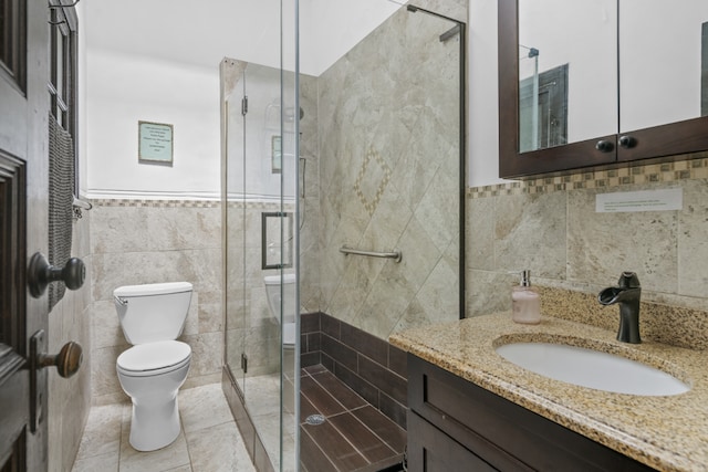 bathroom featuring toilet, vanity, tile walls, tile patterned floors, and a stall shower