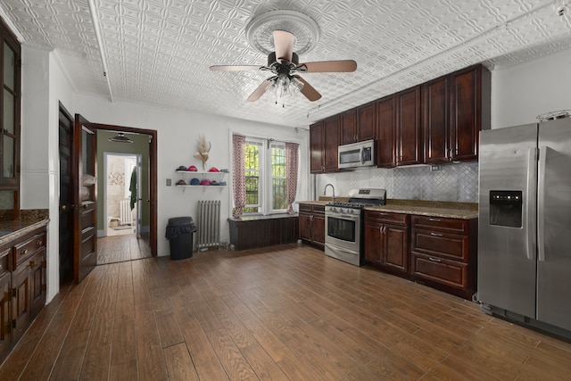 kitchen featuring dark wood-style flooring, ceiling fan, an ornate ceiling, radiator heating unit, and stainless steel appliances