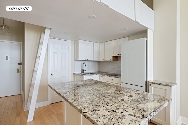 kitchen with sink, white cabinetry, a center island, light stone countertops, and white fridge