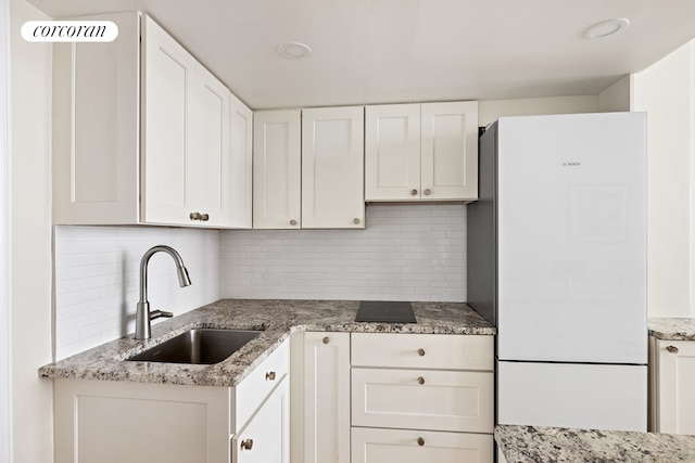 kitchen with a sink, backsplash, white cabinets, and freestanding refrigerator