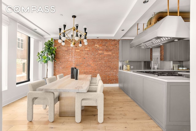 dining area featuring an inviting chandelier, brick wall, baseboards, and light wood-style floors