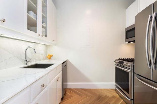 kitchen featuring white cabinets, appliances with stainless steel finishes, light parquet flooring, sink, and light stone counters