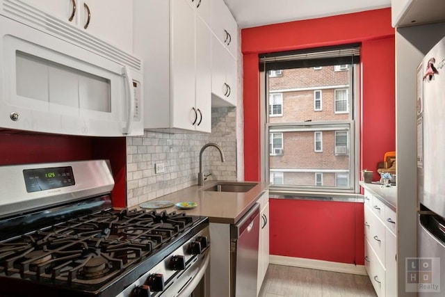 kitchen with tasteful backsplash, light wood-style flooring, white cabinets, stainless steel appliances, and a sink