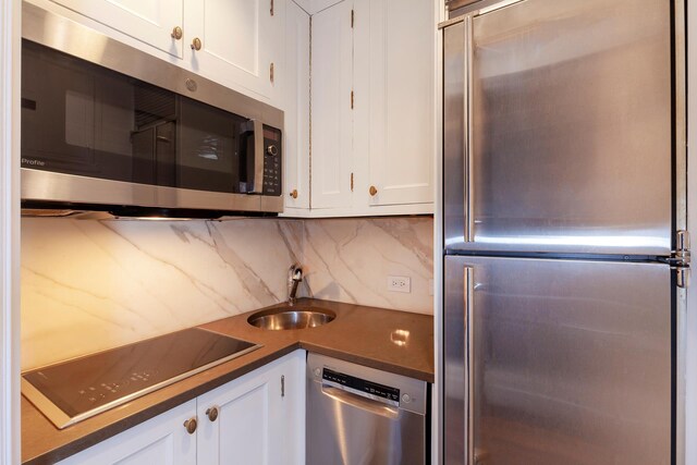 1040 Park Ave Unit 12G2, New York City, NY 10028 - kitchen featuring appliances with stainless steel finishes, white cabinetry, decorative backsplash, dark countertops, and a sink
