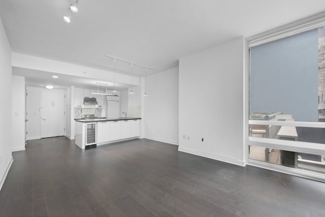 unfurnished living room featuring baseboards, track lighting, beverage cooler, and dark wood finished floors