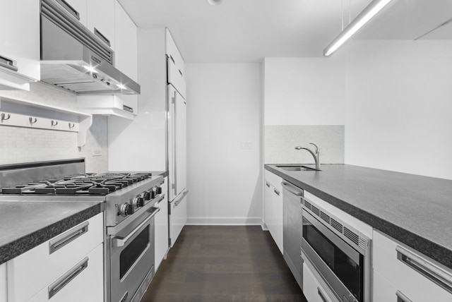 kitchen featuring white cabinets, dark countertops, built in appliances, under cabinet range hood, and a sink