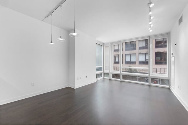 spare room with dark wood-type flooring, visible vents, baseboards, a wall of windows, and rail lighting