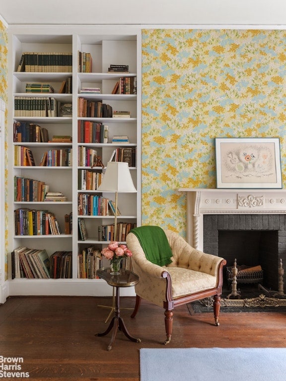 sitting room with dark wood-type flooring, a brick fireplace, and built in shelves