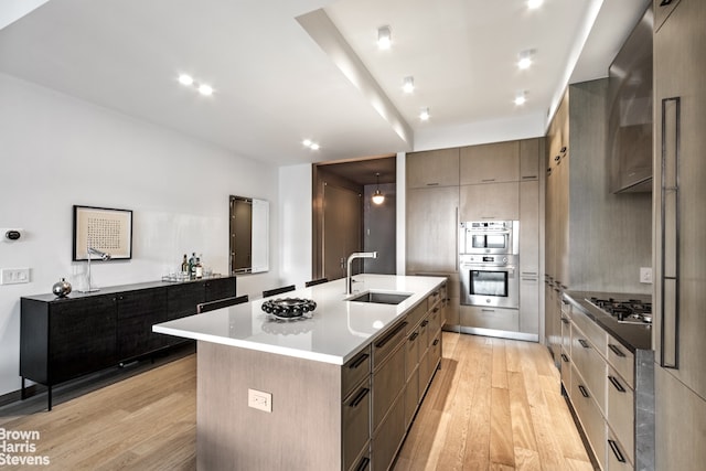 kitchen with stainless steel gas cooktop, sink, a center island with sink, and light hardwood / wood-style flooring