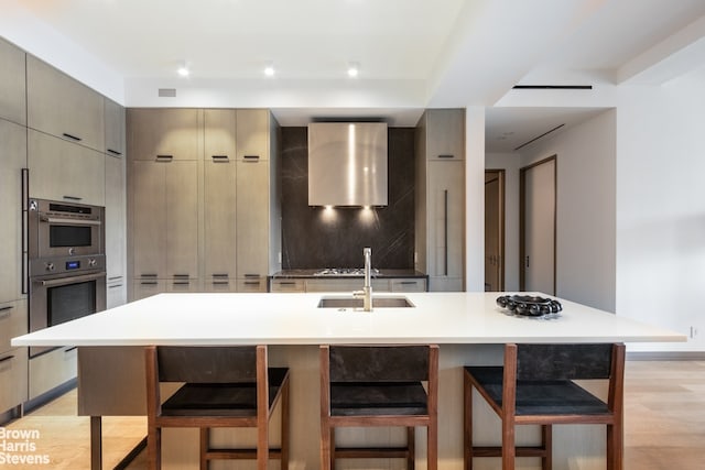 kitchen with gray cabinets, sink, a breakfast bar area, a large island with sink, and light hardwood / wood-style floors