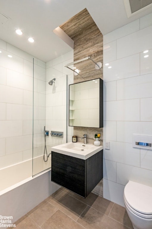 full bathroom with vanity, tiled shower / bath combo, tile walls, and toilet