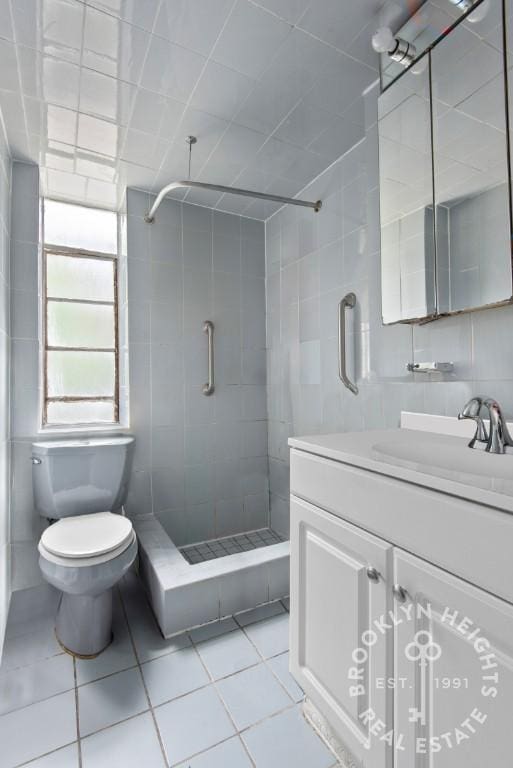 bathroom featuring tile patterned floors, toilet, a stall shower, tile walls, and vanity