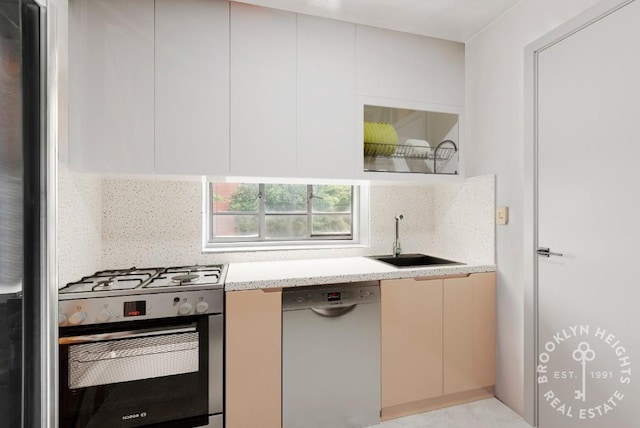 kitchen with light stone counters, backsplash, stainless steel gas stove, a sink, and dishwasher