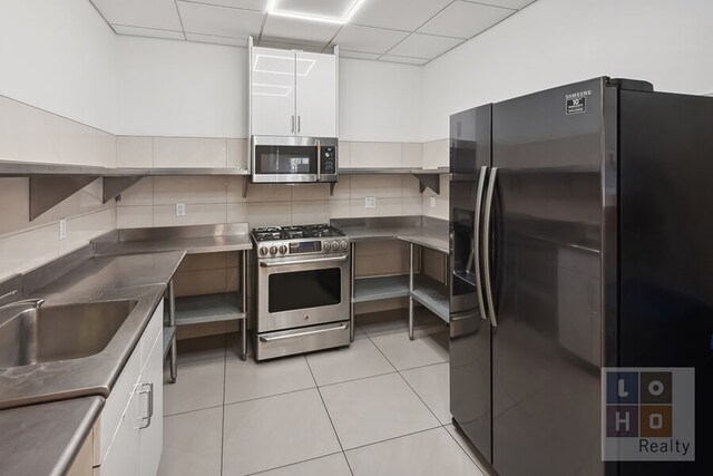 266 E Broadway Unit B606, New York City, NY 10002 - kitchen featuring stainless steel countertops, appliances with stainless steel finishes, white cabinetry, a drop ceiling, and light tile patterned floors