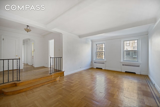 spare room featuring baseboards, arched walkways, beamed ceiling, and radiator heating unit