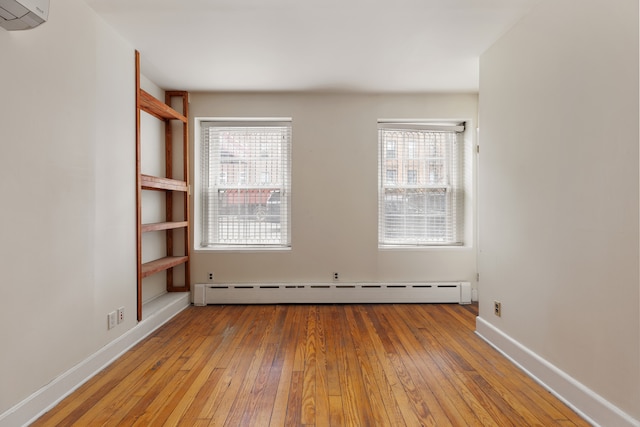 spare room with a healthy amount of sunlight, a wall mounted air conditioner, baseboards, and wood-type flooring