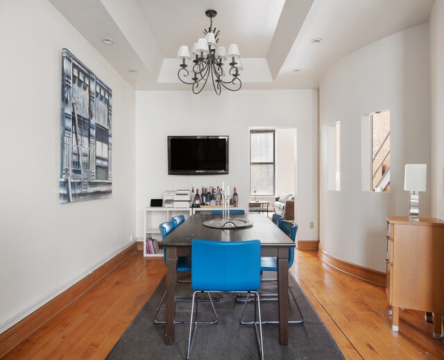 dining area featuring a notable chandelier, baseboards, a tray ceiling, and hardwood / wood-style floors